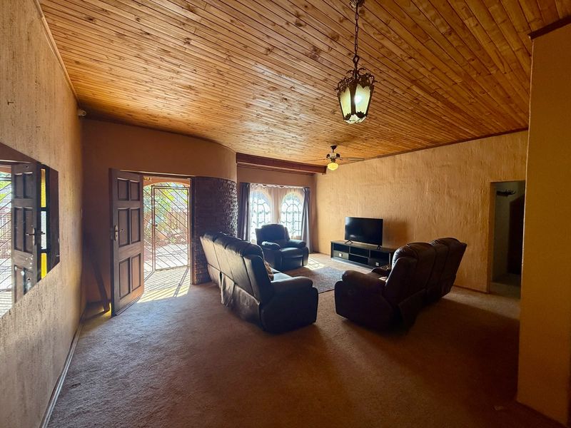Spacious living room featuring a timber-clad ceiling, textured walls, and arched windows, providing a rustic aesthetic with potential for modern updates.