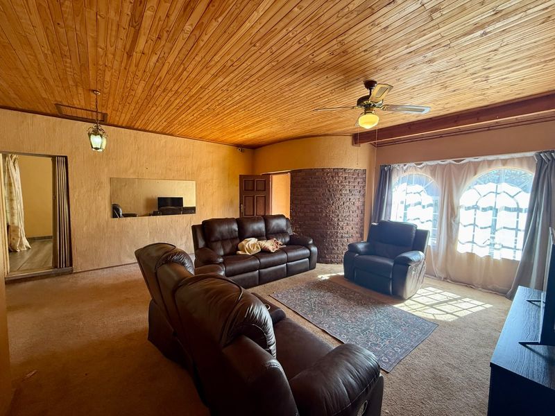 Spacious living room featuring a warm timber-clad ceiling, exposed brick accent wall, and large arched windows that provide ample natural light.