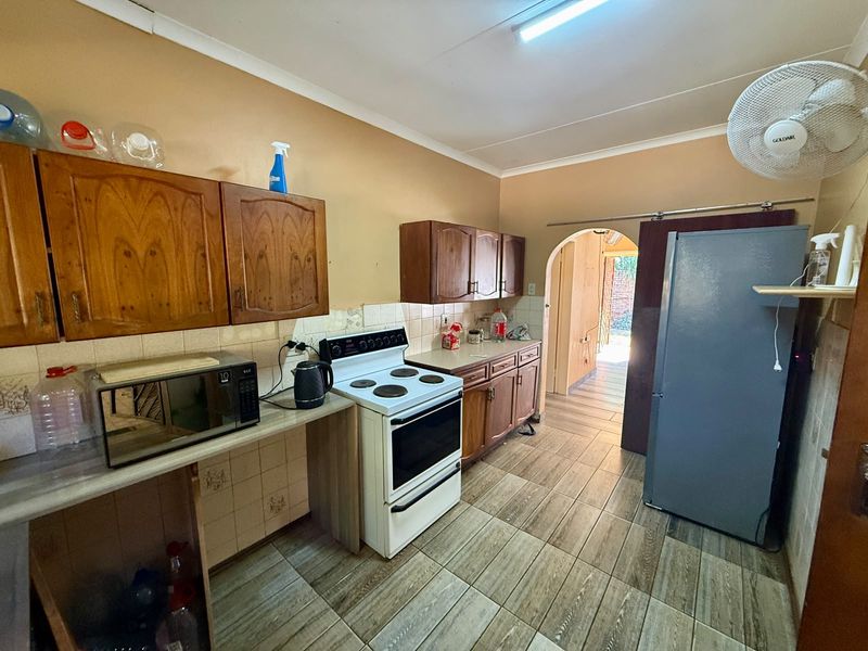 A functional kitchen featuring wooden cabinetry, tiled backsplash, and tiled flooring, with an arched doorway leading to an adjacent space.