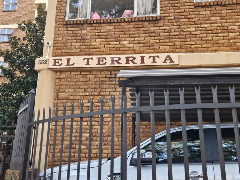 Exterior view of the El Territa apartment building featuring a brick facade, security fencing, and a covered carport area.