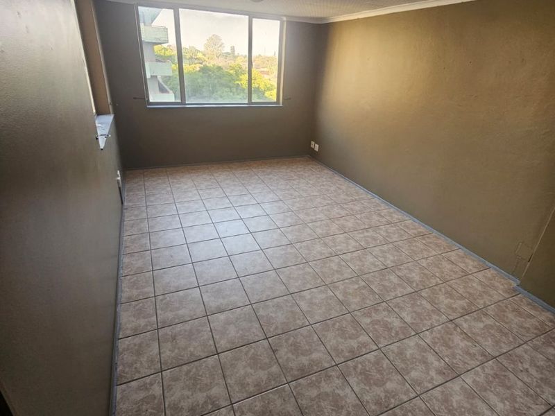 An empty living room featuring tiled flooring, a textured ceiling, and a large window providing natural light and an exterior view.