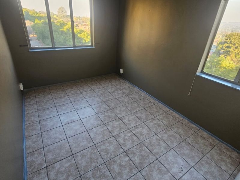An empty bedroom featuring tiled flooring, neutral wall paint, and large windows providing natural light and elevated views.