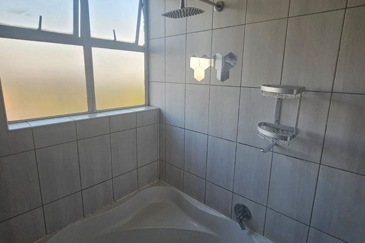 A bathroom featuring a corner bathtub with a wall-mounted shower head and tiled wall finishes, illuminated by a large window.