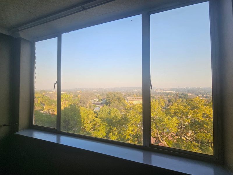 A view from an apartment window overlooking a suburban landscape with mature trees and distant buildings.