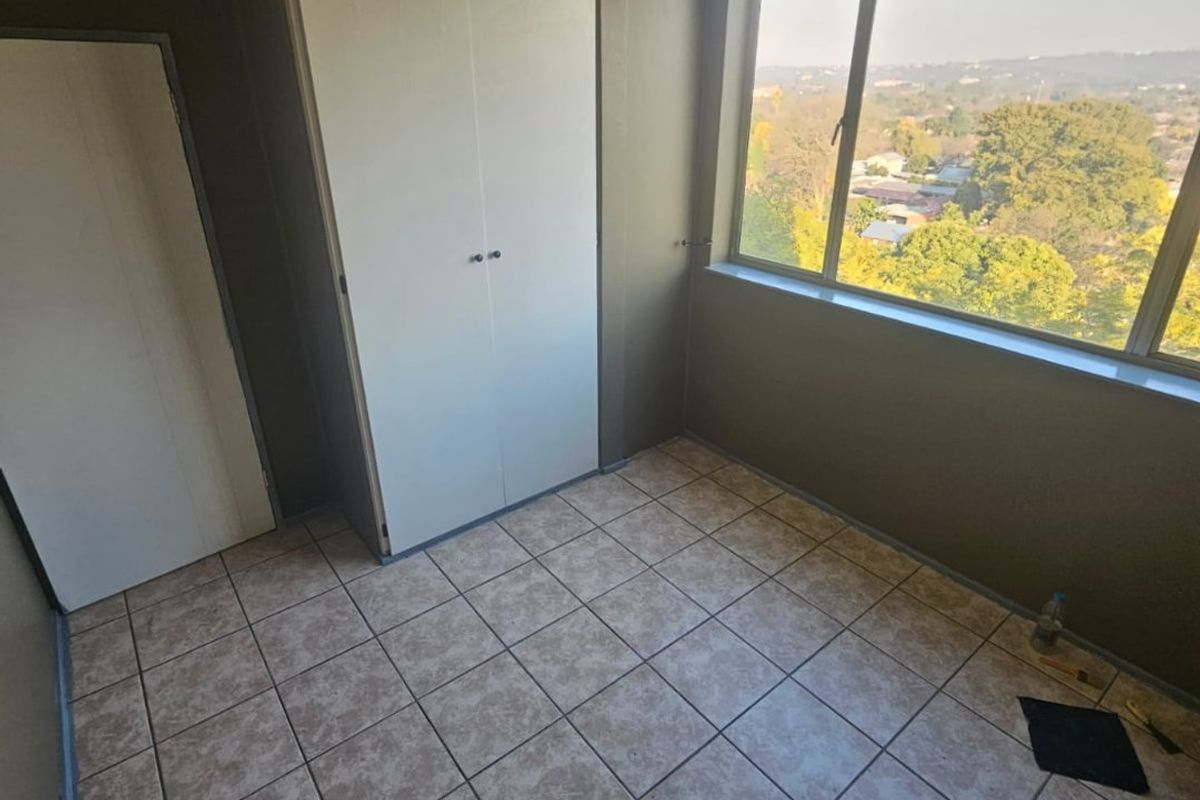 An empty bedroom featuring tiled flooring, a built-in cupboard, and a large window offering an elevated view of the surrounding area.