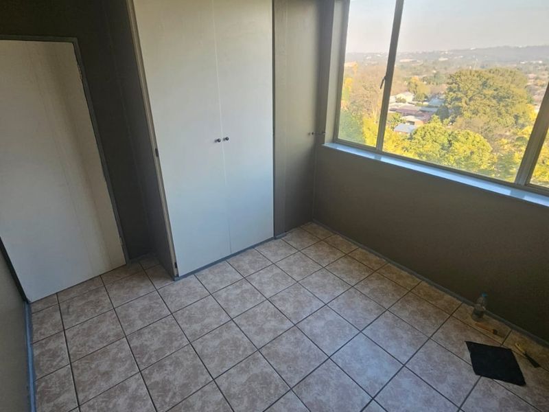 An empty bedroom featuring tiled flooring, a built-in cupboard, and a large window offering an elevated view of the surrounding area.