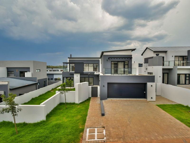 Modern double-story residential property featuring a paved driveway, double garage, and a balcony with glass balustrades, set within a contemporary estate.