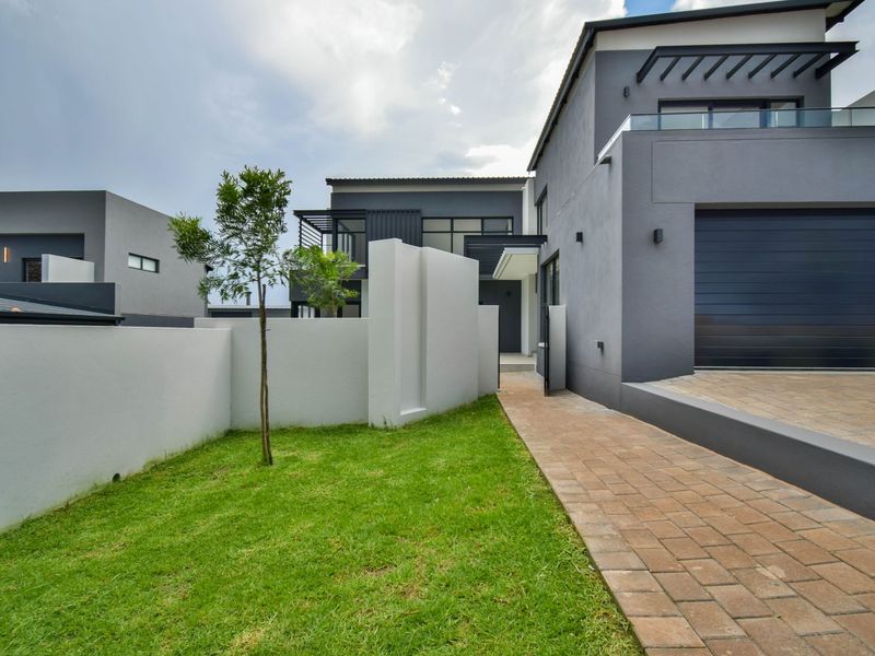 Modern contemporary home exterior featuring a paved driveway, integrated garage, and clean architectural lines with a landscaped front garden.