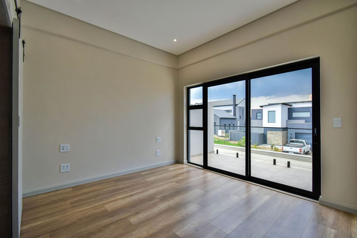 A bright, empty bedroom featuring modern laminate flooring, recessed lighting, and large sliding glass doors that open onto a private balcony.