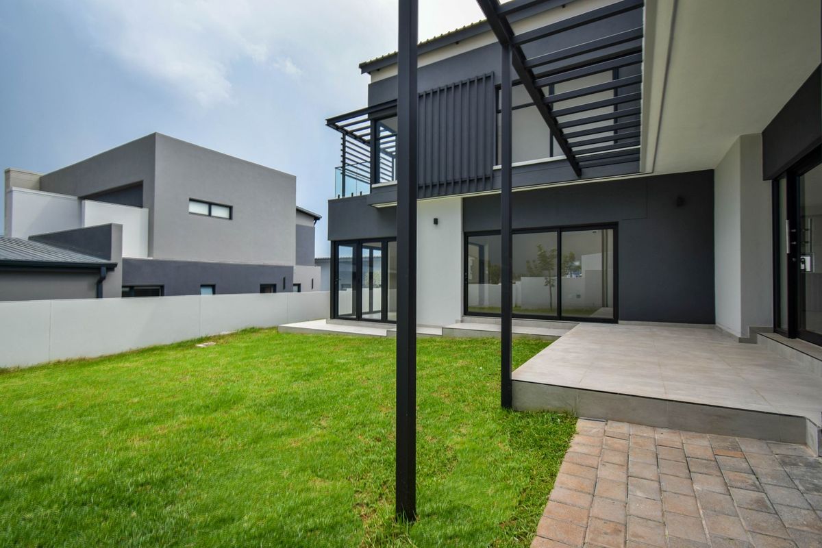 Modern rear exterior featuring a tiled patio, pergola structure, and sliding glass doors overlooking a private lawn and boundary wall.