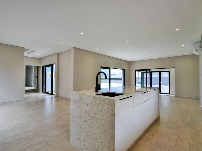 Spacious open-plan living area featuring a modern kitchen island with stone countertops, sleek black fixtures, tiled flooring, and large sliding doors for natural light.