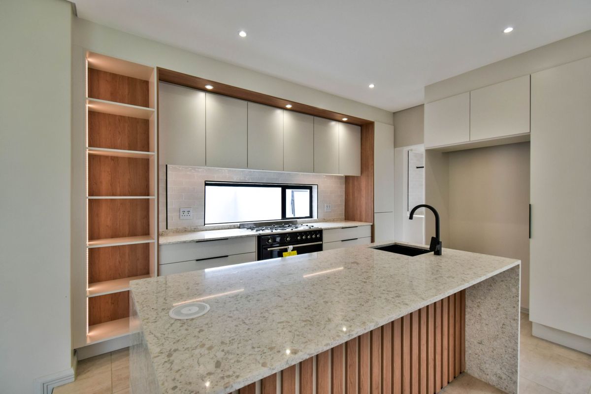 Modern kitchen featuring a large stone-topped island, gas stove, sleek cabinetry with integrated lighting, and high-quality finishes throughout.