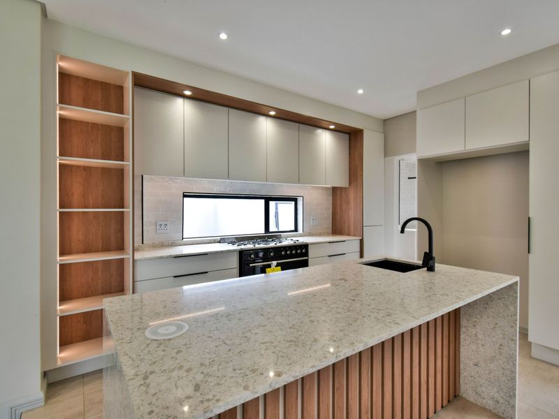 Modern kitchen featuring a large stone-topped island, gas stove, sleek cabinetry with integrated lighting, and high-quality finishes throughout.