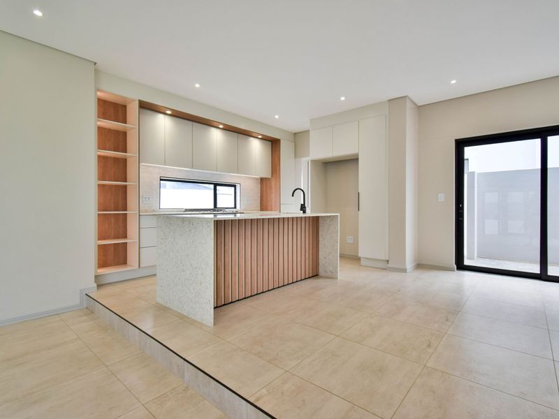 Modern open-plan kitchen featuring a central island with stone countertop, sleek built-in cabinetry, recessed lighting, and direct access to the outdoor area.