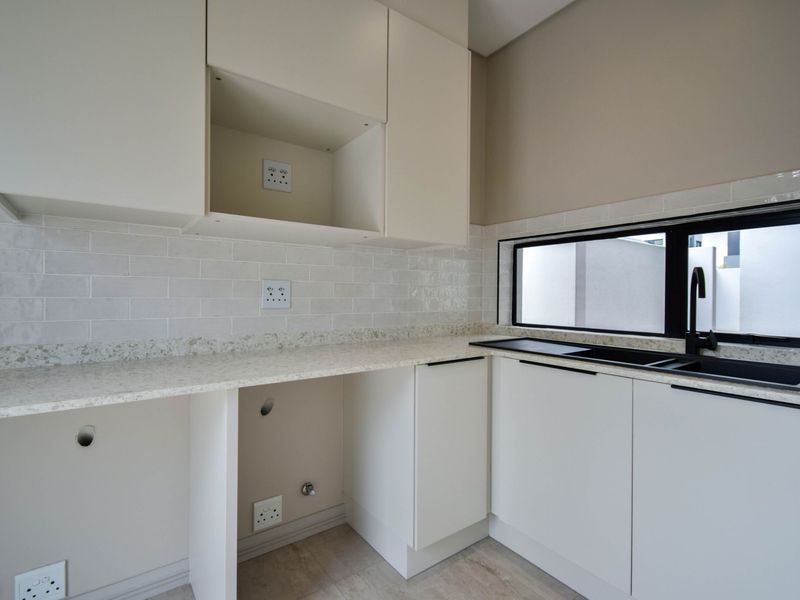 A modern, clean scullery featuring stone countertops, subway tile backsplash, built-in cabinetry, and a black sink with matching tapware.