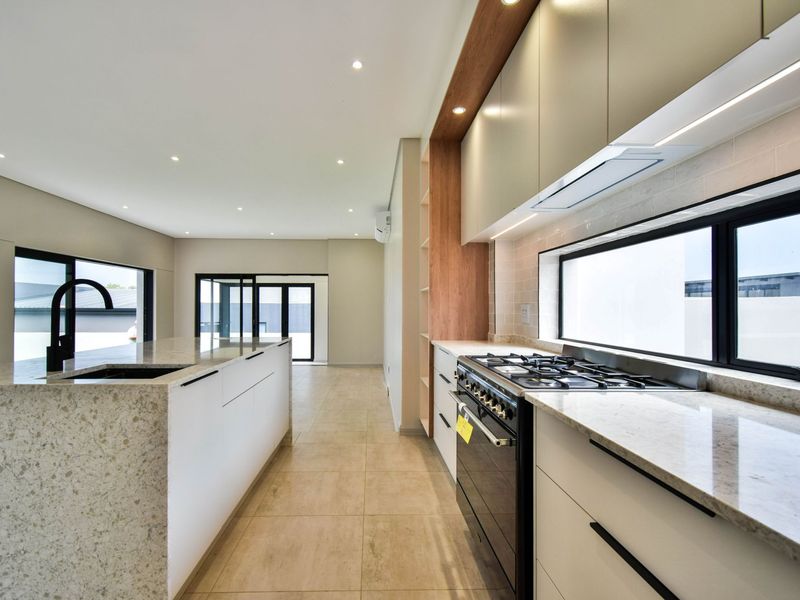 Modern kitchen featuring a large stone-topped island, gas stove, sleek cabinetry, and recessed lighting, flowing into an open-plan living area with sliding glass doors.