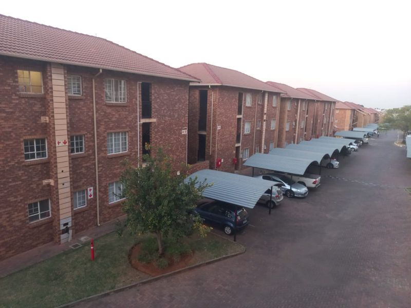 Exterior view of a multi-story apartment complex featuring face brick construction, tiled roofing, and dedicated covered carport parking bays for residents.