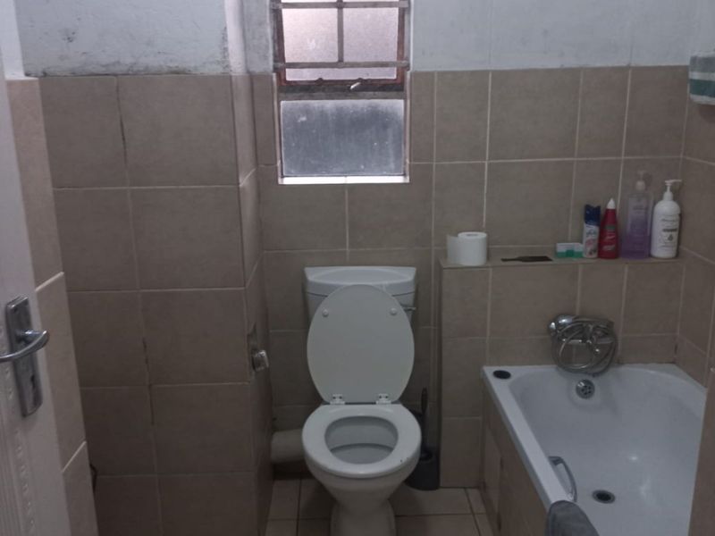 A compact bathroom featuring a standard bathtub, toilet, and neutral wall tiling. The space requires cosmetic updates to the wall finishes and fixtures.