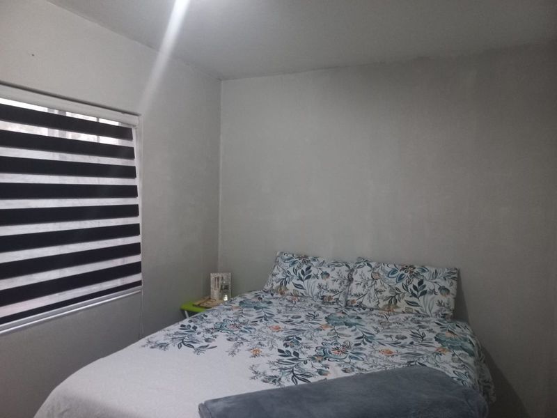 A simple bedroom featuring neutral walls and modern striped roller blinds, providing a functional and private sleeping space.