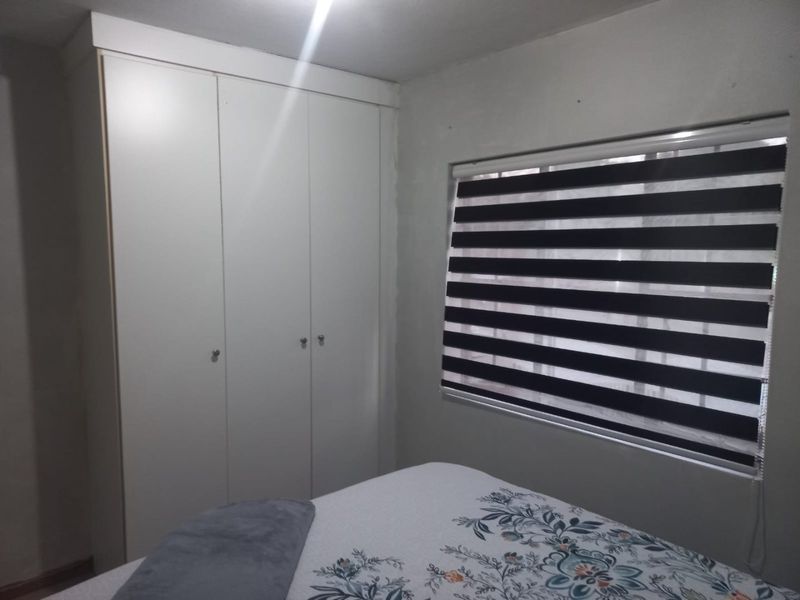 A bedroom featuring a white built-in wardrobe and modern zebra-style window blinds.