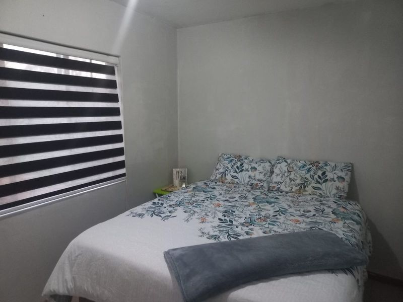 A simple bedroom featuring neutral walls and modern zebra-style window blinds.