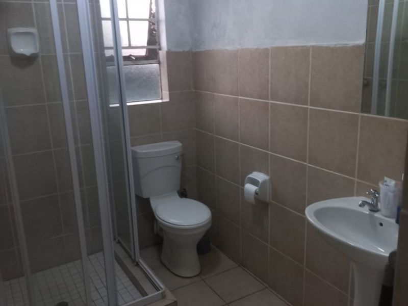 A functional bathroom featuring a shower enclosure, pedestal basin, and toilet with neutral wall and floor tiling.