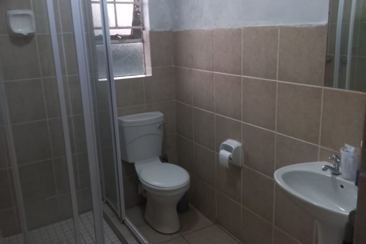 A functional bathroom featuring a shower enclosure, pedestal basin, and toilet with neutral wall and floor tiling.