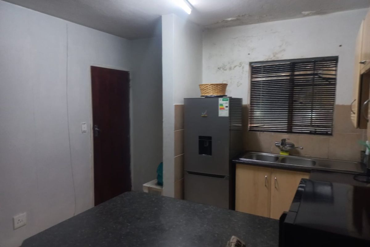 A compact kitchen featuring laminate cabinetry, a double sink, and a dark countertop, currently showing signs of water damage on the walls and ceiling.