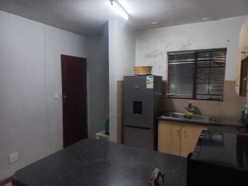 A compact kitchen featuring laminate cabinetry, a double sink, and a dark countertop, currently showing signs of water damage on the walls and ceiling.