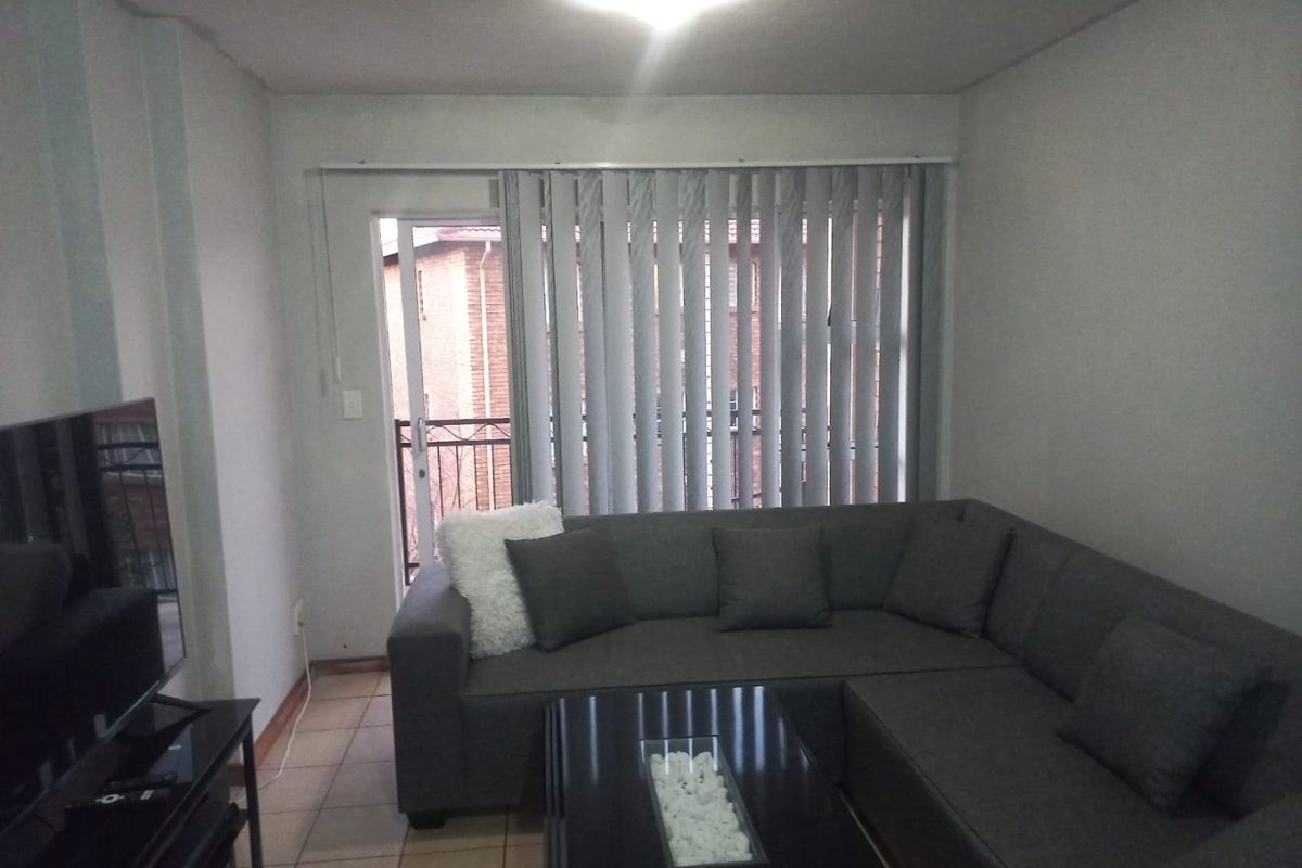 A living room featuring tiled flooring, vertical blinds, and a sliding glass door leading to an outdoor area.