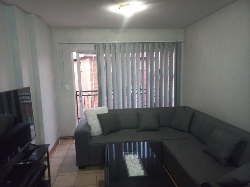 A living room featuring tiled flooring, vertical blinds, and a sliding glass door leading to an outdoor area.