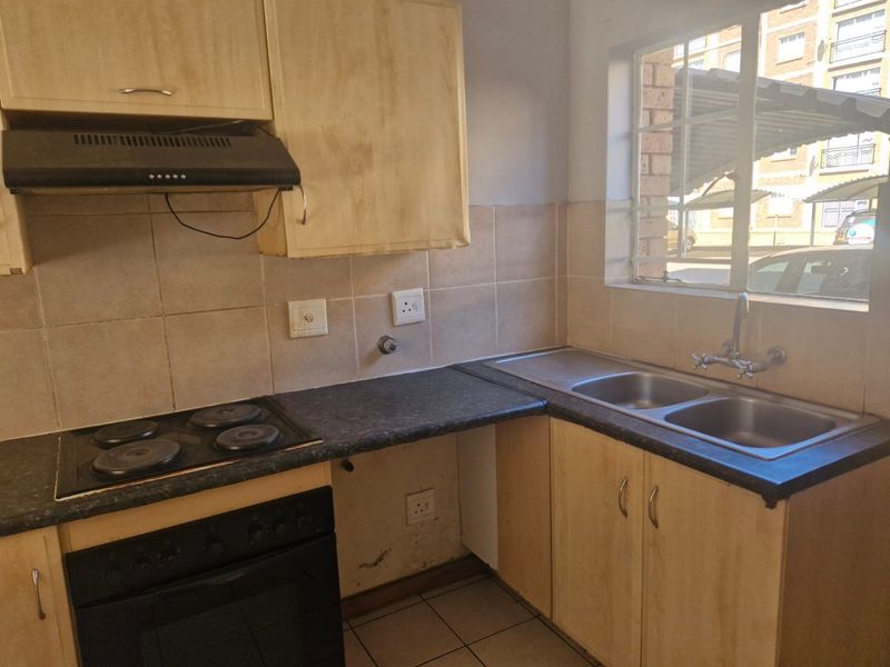 A functional kitchen featuring laminate cabinetry, a double bowl stainless steel sink, electric hob, and built-in oven with tiled splashback.