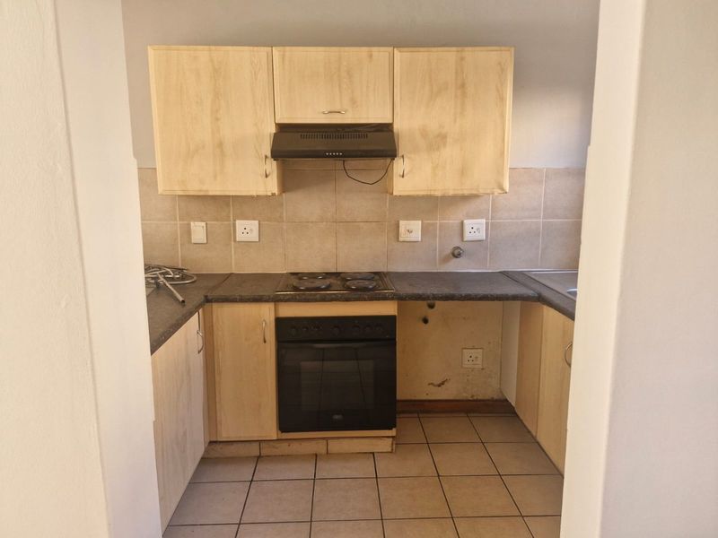 A compact kitchen featuring built-in cabinetry, an electric oven and hob, tiled backsplash, and ceramic floor tiles, currently requiring some maintenance and cosmetic updates.