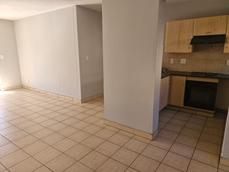 An open-plan living and kitchen area featuring tiled flooring and functional built-in cabinetry with integrated oven and hob.