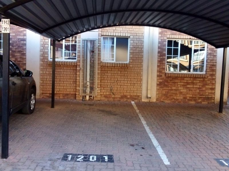 A designated covered parking bay with brick paving and a metal carport structure located in front of the apartment building.