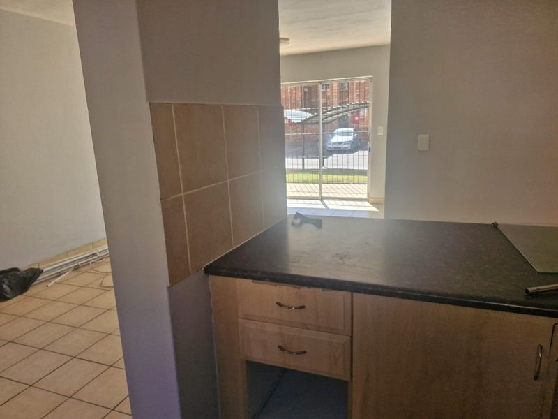 A compact kitchen area featuring laminate cabinetry, dark countertops, and ceramic tiling, with an open layout leading to an exterior sliding door.