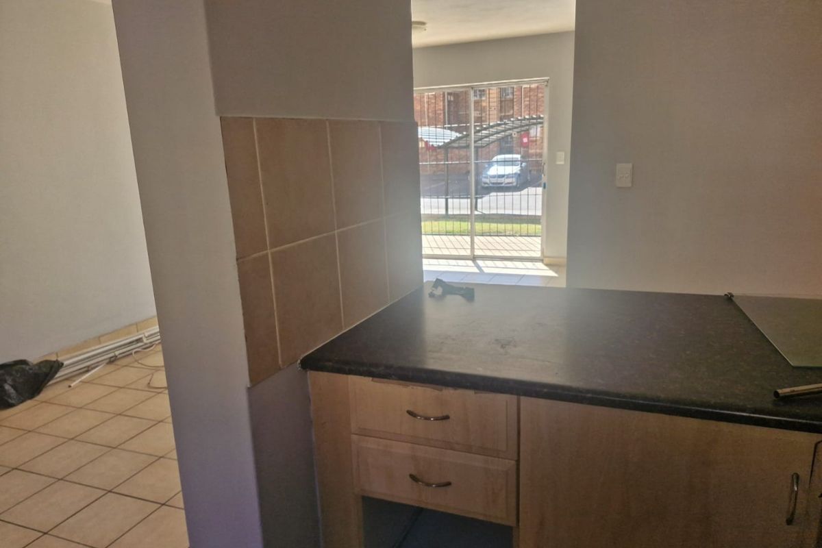 A compact kitchen area featuring laminate cabinetry, dark countertops, and ceramic tiling, with an open layout leading to an exterior sliding door.