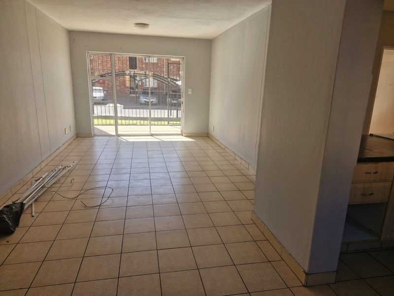 An empty open-plan living area featuring ceramic tiled flooring and a sliding glass door with security gate, leading to an exterior view.