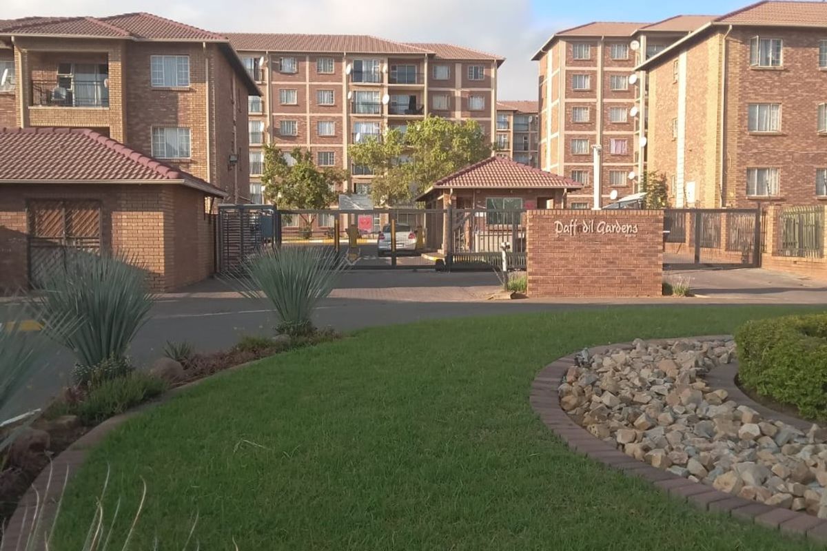 Front entrance view of Daffodil Gardens apartment complex featuring brick buildings, secure gated access, and well-maintained landscaped gardens.