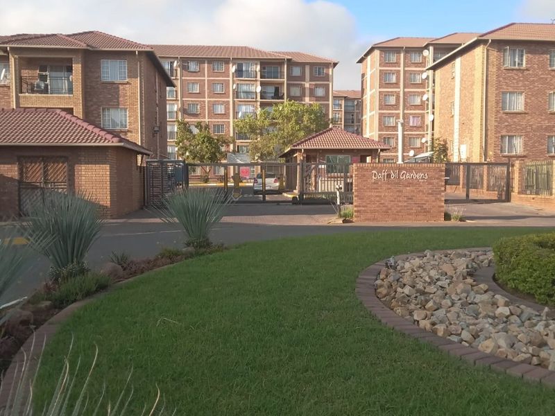 Front entrance view of Daffodil Gardens apartment complex featuring brick buildings, secure gated access, and well-maintained landscaped gardens.
