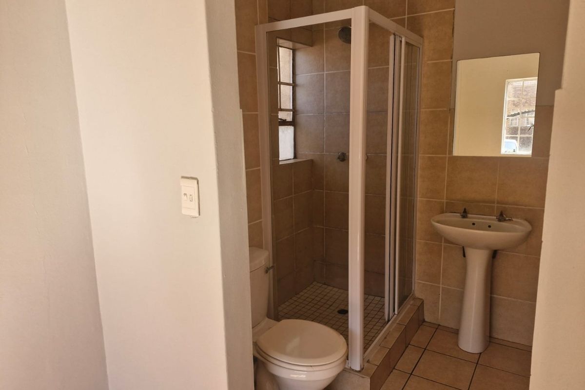 A functional bathroom featuring a shower enclosure, pedestal basin, and toilet with neutral wall and floor tiling.