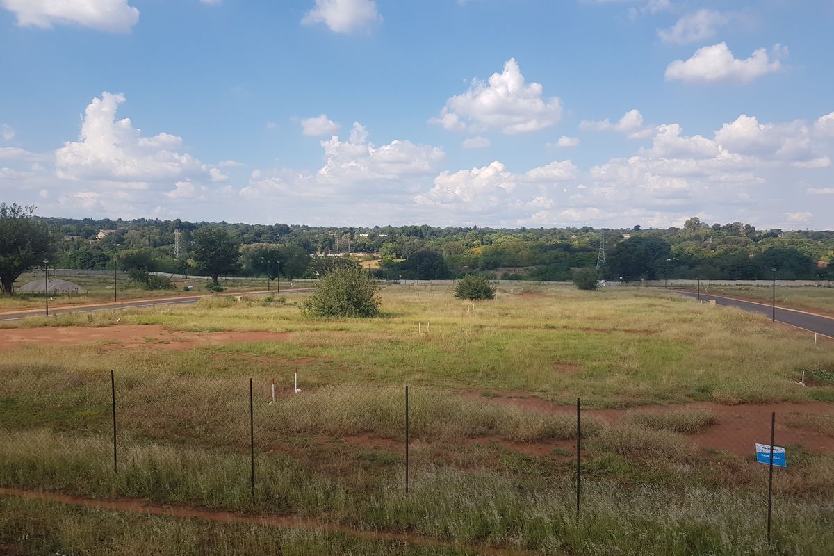 A vacant residential plot featuring open grass, wire fencing, and established road access, offering a clear view of the surrounding landscape.