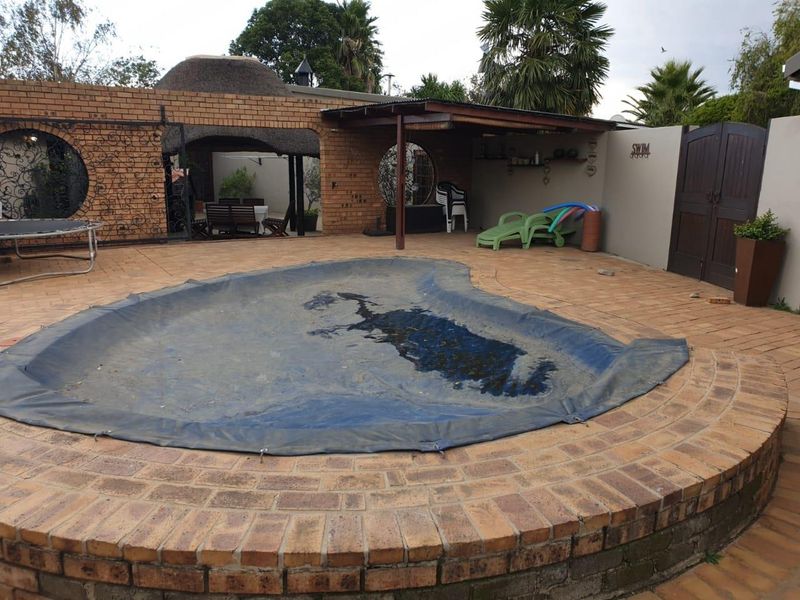 Outdoor pool area featuring a brick-paved patio, covered entertainment space, and a thatched roof structure, ideal for relaxed outdoor living.