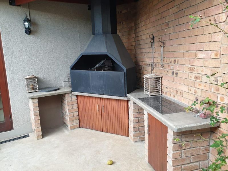 Covered outdoor patio area featuring a built-in brick braai with a metal hood, concrete countertops, and integrated storage cabinetry.