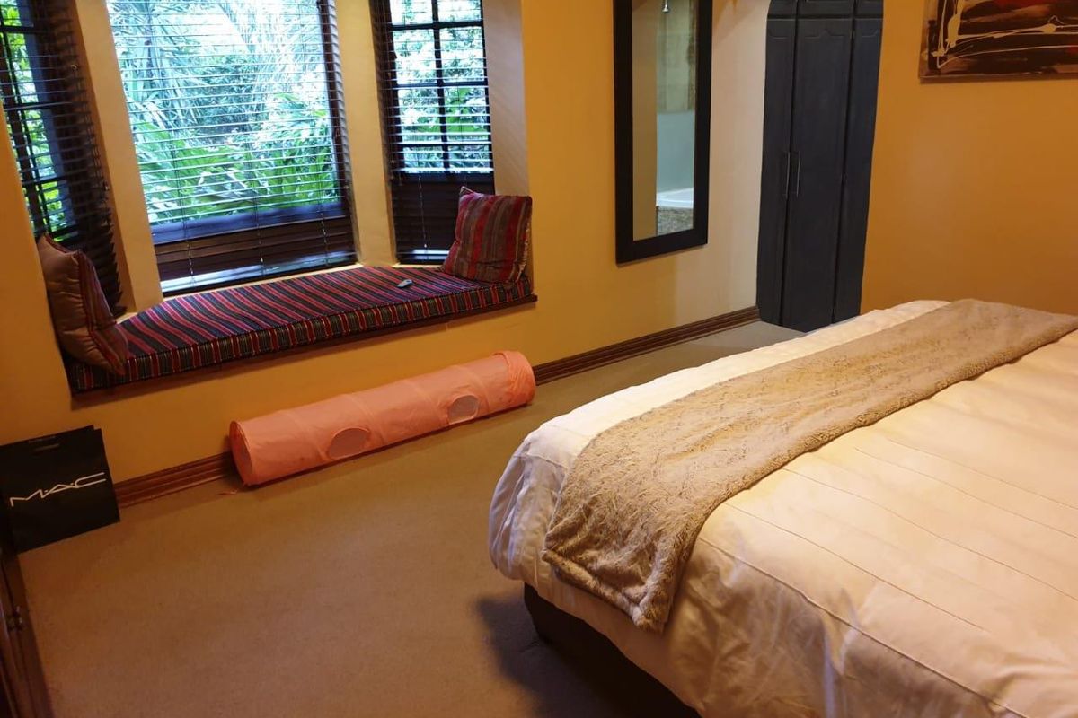 A cozy bedroom featuring a built-in window seat with wooden blinds, carpeted flooring, and an arched doorway leading to an adjoining space.