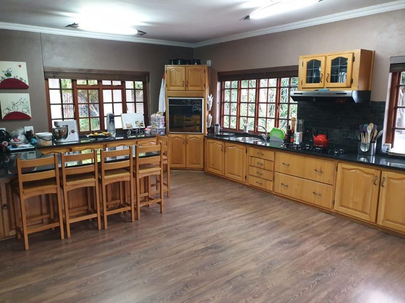 Spacious kitchen featuring wooden cabinetry, dark granite countertops, a built-in oven, gas hob, and an integrated breakfast bar area with large windows.