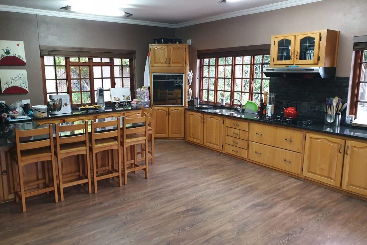 Spacious kitchen featuring wooden cabinetry, dark granite countertops, a built-in oven, gas hob, and an integrated breakfast bar area with large windows.