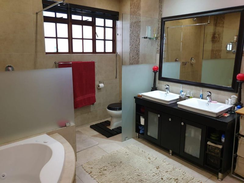 A functional bathroom featuring a double vanity with dark cabinetry, a corner soaking tub, a toilet, and a glass-enclosed shower area.