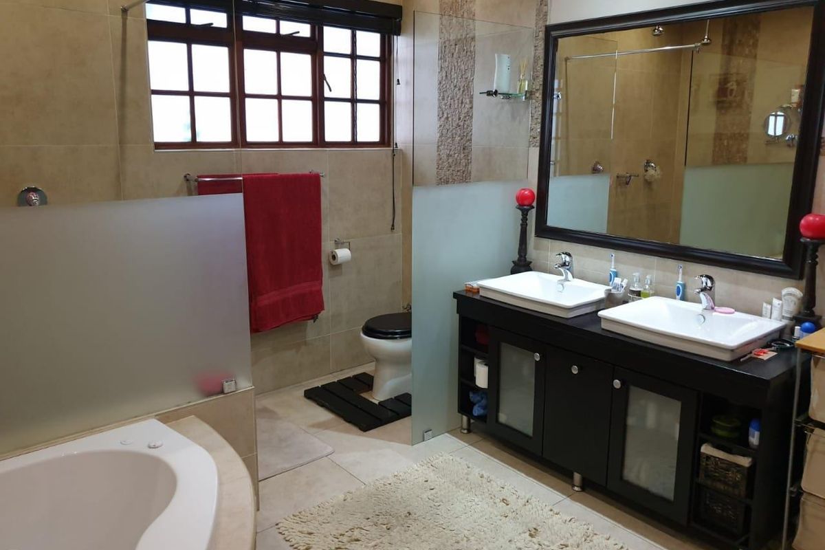A functional bathroom featuring a double vanity with dark cabinetry, a corner soaking tub, a toilet, and a glass-enclosed shower area.