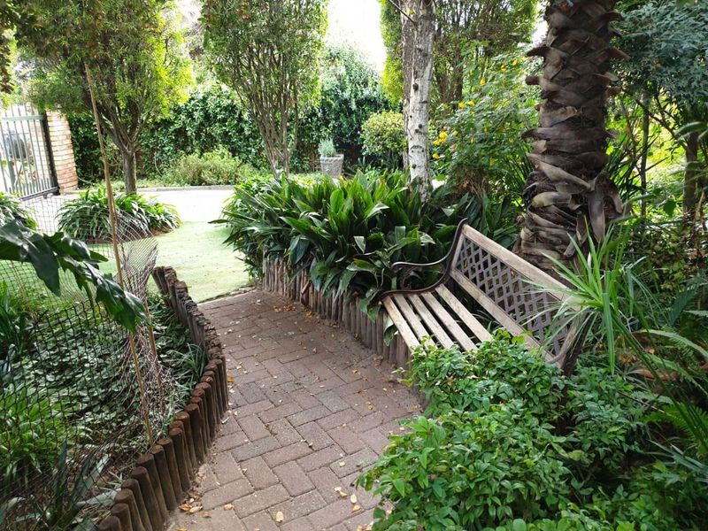 A landscaped garden path featuring brick paving, established trees, and mature shrubbery, creating a secluded outdoor walkway.